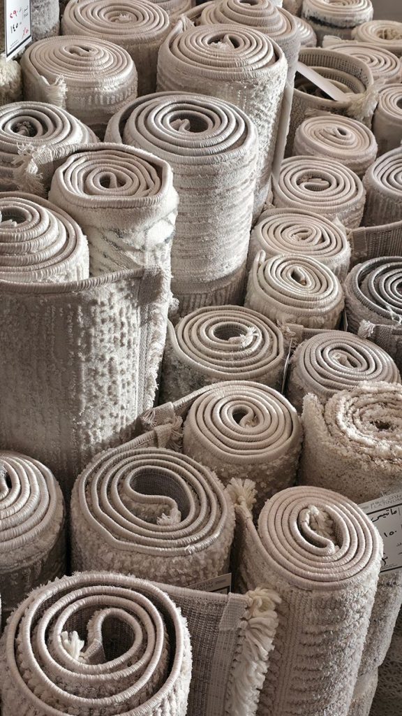team-02 Elegant rolled carpets neatly stacked in a Jeddah market, showcasing intricate textures and neutral tones.